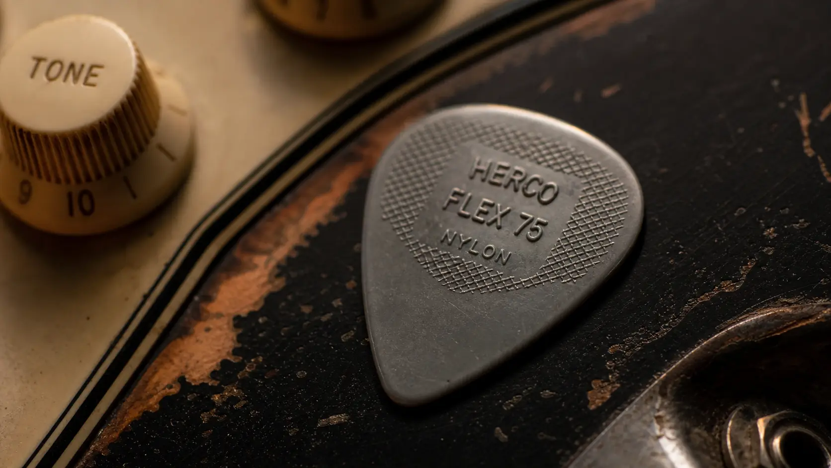 Gros plan sur un médiator gris posé sur le corps noir d'une guitare Fender Stratocaster